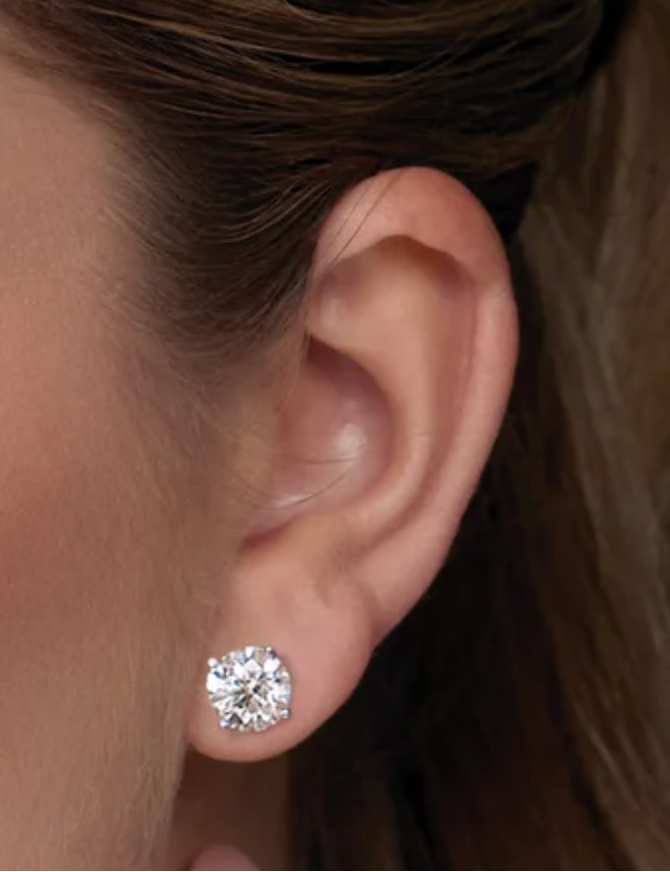 Close-up of an ear wearing a diamond stud earring with hair partially covering the frame.